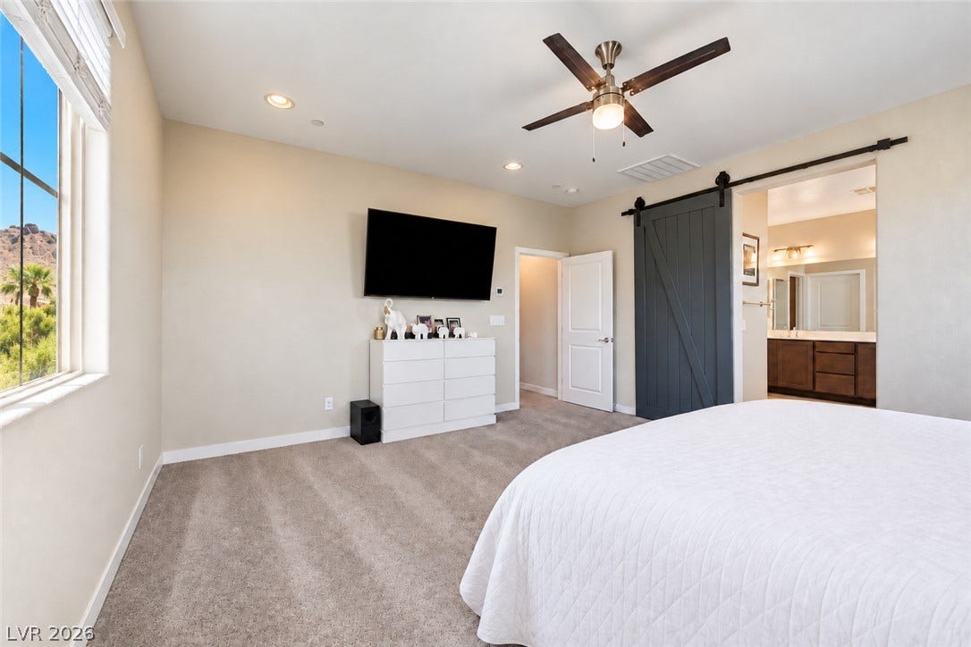 31 Cresta Villa Court, Henderson, NV 89011 A sliding barn door leads to the en suite bathroom in this comfortable carpeted bedroom.