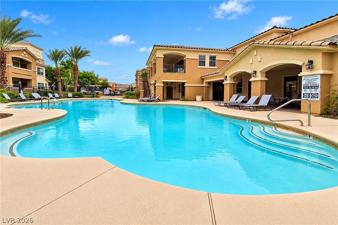 8777 W Maule Avenue, #2109, Las Vegas, NV 89148 A pristine community pool glistens under blue skies, flanked by Spanish-style multi-level residential structures.