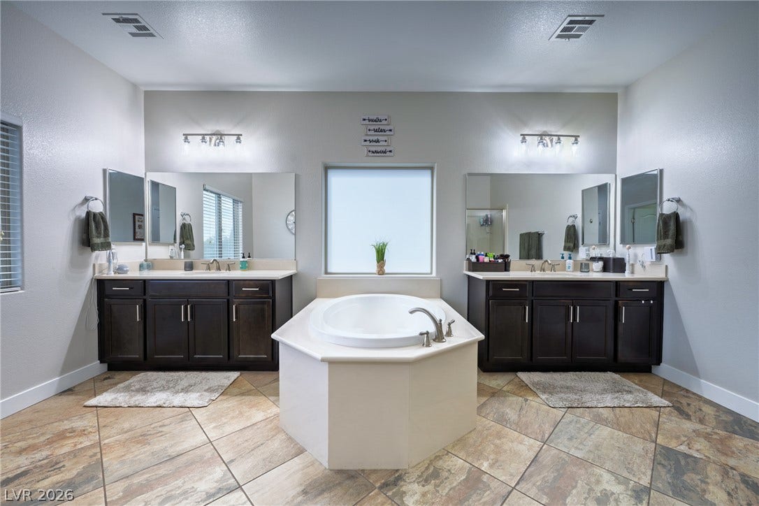 152 Dunblane Street, Henderson, NV 89012 A spacious layout features dual dark wood vanities alongside a central soaking tub and tile flooring.