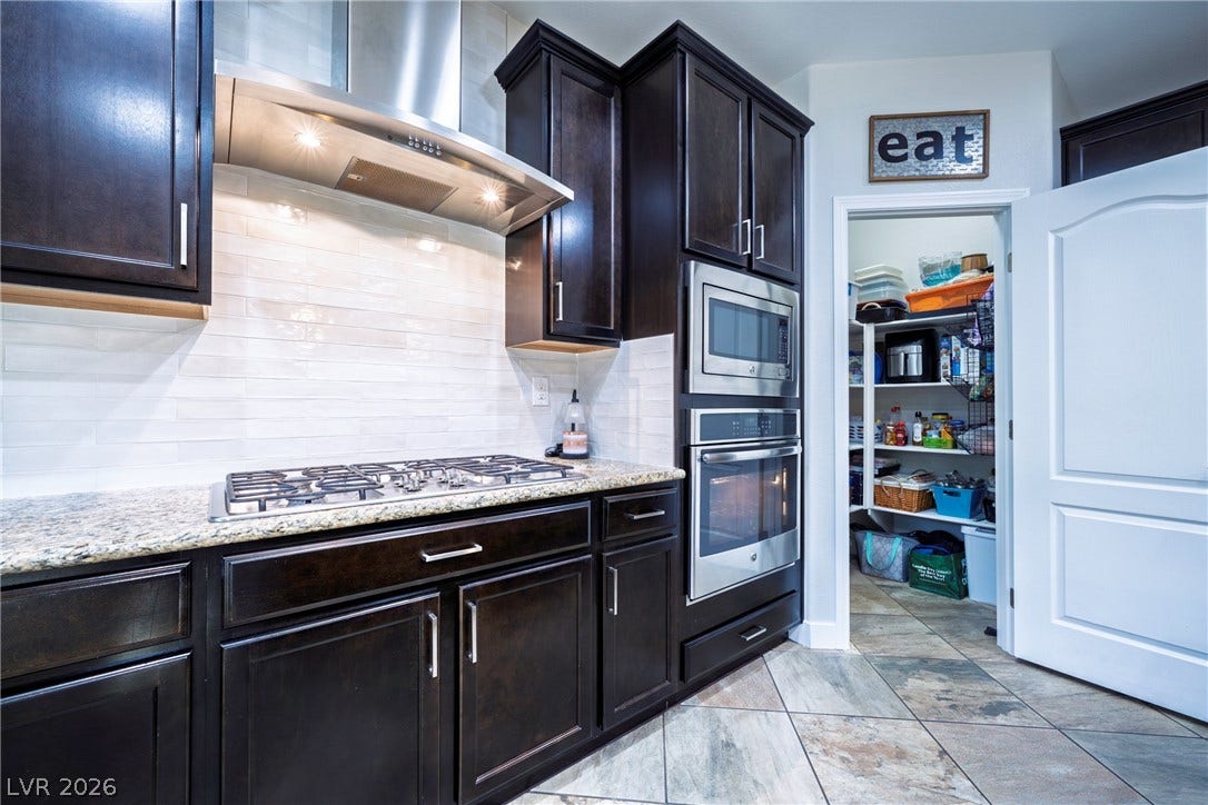 152 Dunblane Street, Henderson, NV 89012 Rich dark cabinetry and granite countertops frame a built-in cooktop and convenient walk-in pantry.