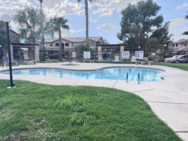 Manicured green lawn borders a crystal blue community swimming pool under a bright sky.