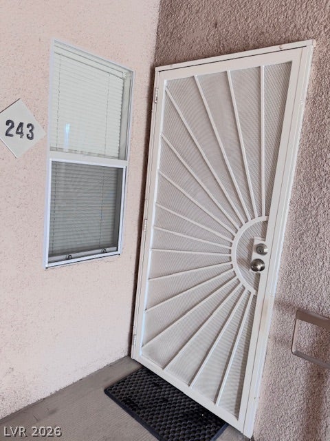 A sturdy security screen door stands alongside a multi-pane window against textured stucco walls.
