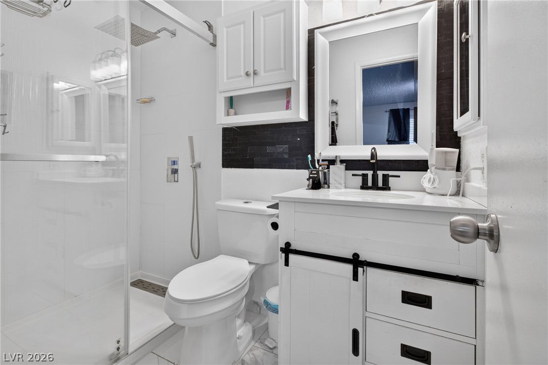1341 Pinto Rock Lane, #202, Las Vegas, NV 89128 A glass-enclosed shower alongside a modern single vanity with dark tile backsplashes.