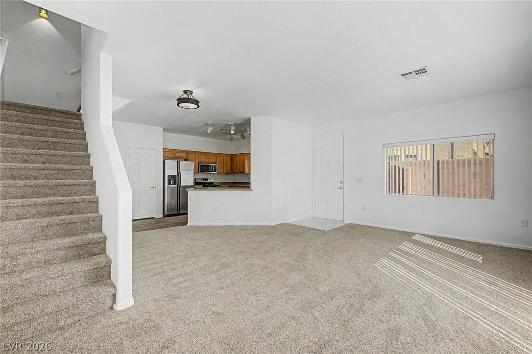 Plush carpeting anchors this versatile living area featuring seamless transitions into the kitchen.