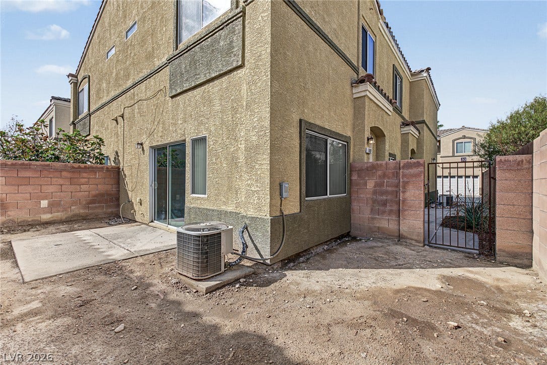 Multi-level stucco exterior showcases a concrete patio slab alongside a fenced yard area.