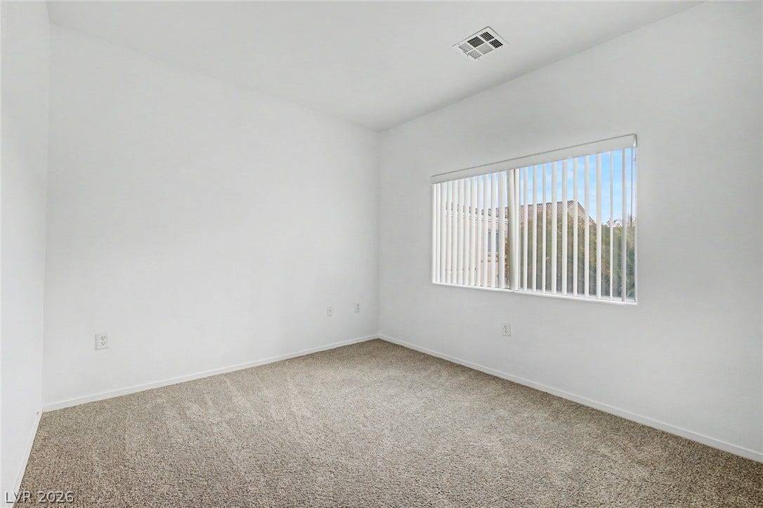 A windowed room features neutral carpeting and clean white walls.
