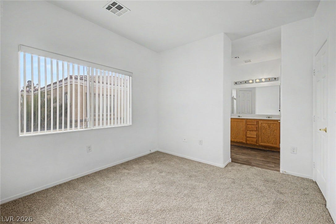 Plush carpet and a large window define this bedroom leading directly to an attached bathroom.
