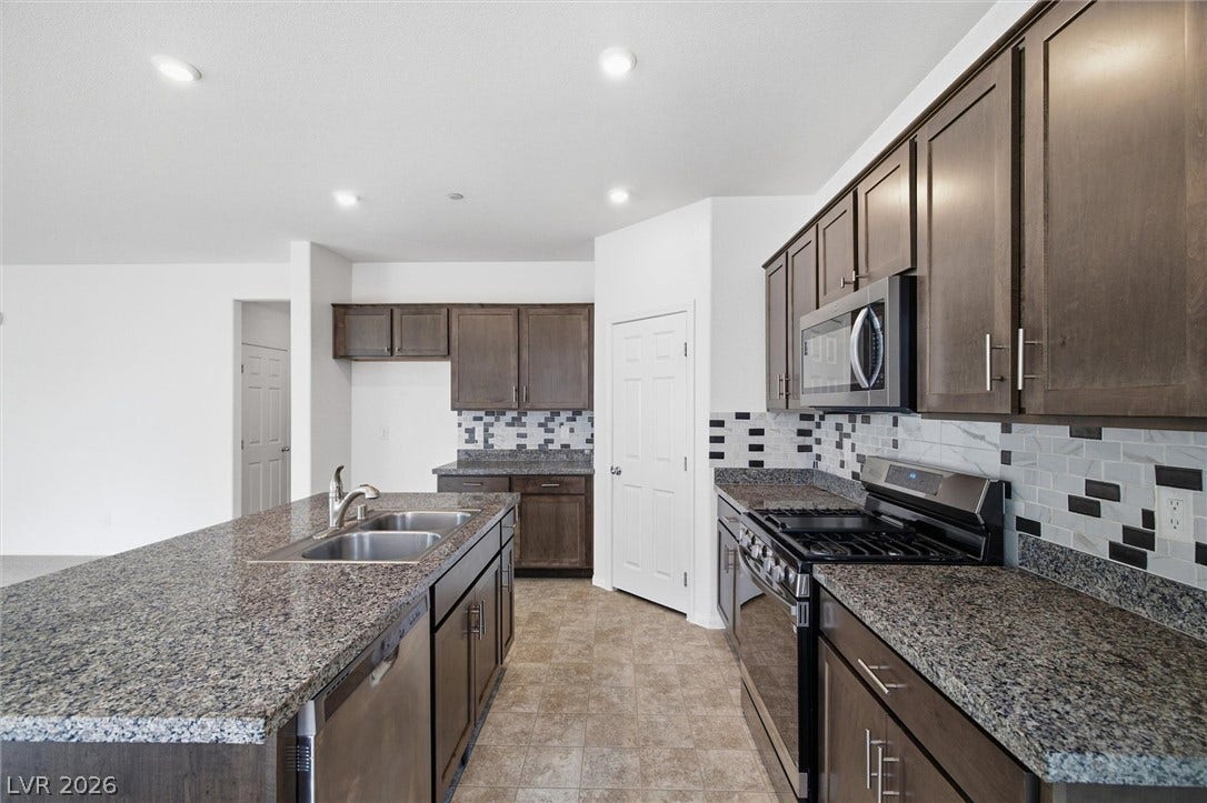 6047 Castle Gardens Avenue, Las Vegas, NV 89130 Gleaming granite countertops pair beautifully with dark wood cabinetry and a central prep island.