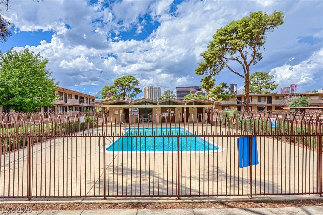 615 S Royal Crest Circle, #16, Las Vegas, NV 89169 A fenced community swimming pool sits beneath towering trees and a dramatic sky.