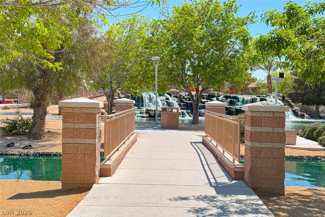 2906 Pumpkin Harvest Avenue, North Las Vegas, NV 89031 A paved bridge crosses tranquil waterways leading toward a scenic cascading rock waterfall.