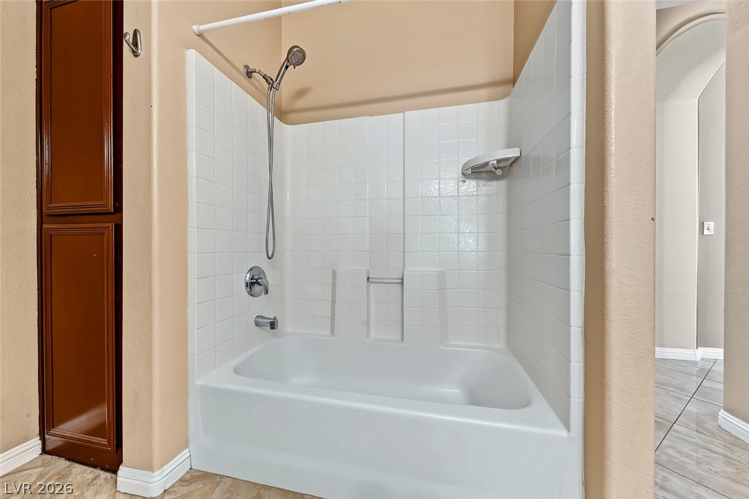 2906 Pumpkin Harvest Avenue, North Las Vegas, NV 89031 White tiled surround framing the bathtub insert is set next to built-in linen storage.