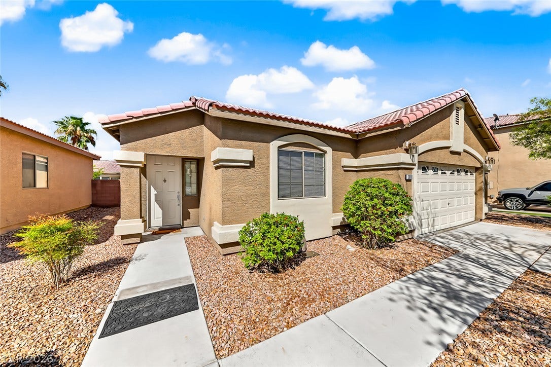 2906 Pumpkin Harvest Avenue, North Las Vegas, NV 89031 A paved concrete walkway leads past desert landscaping to the front entrance of this stucco home.