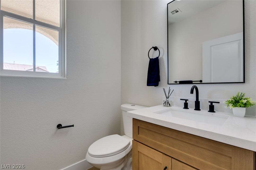 197 Sicily Hills Court, Henderson, NV 89012 Natural light fills this powder room highlighting a wood vanity and stone counter.