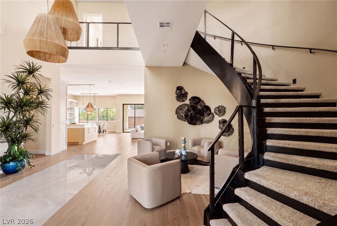 An architectural curved staircase overlooks a spacious foyer with sleek wood and tile flooring.