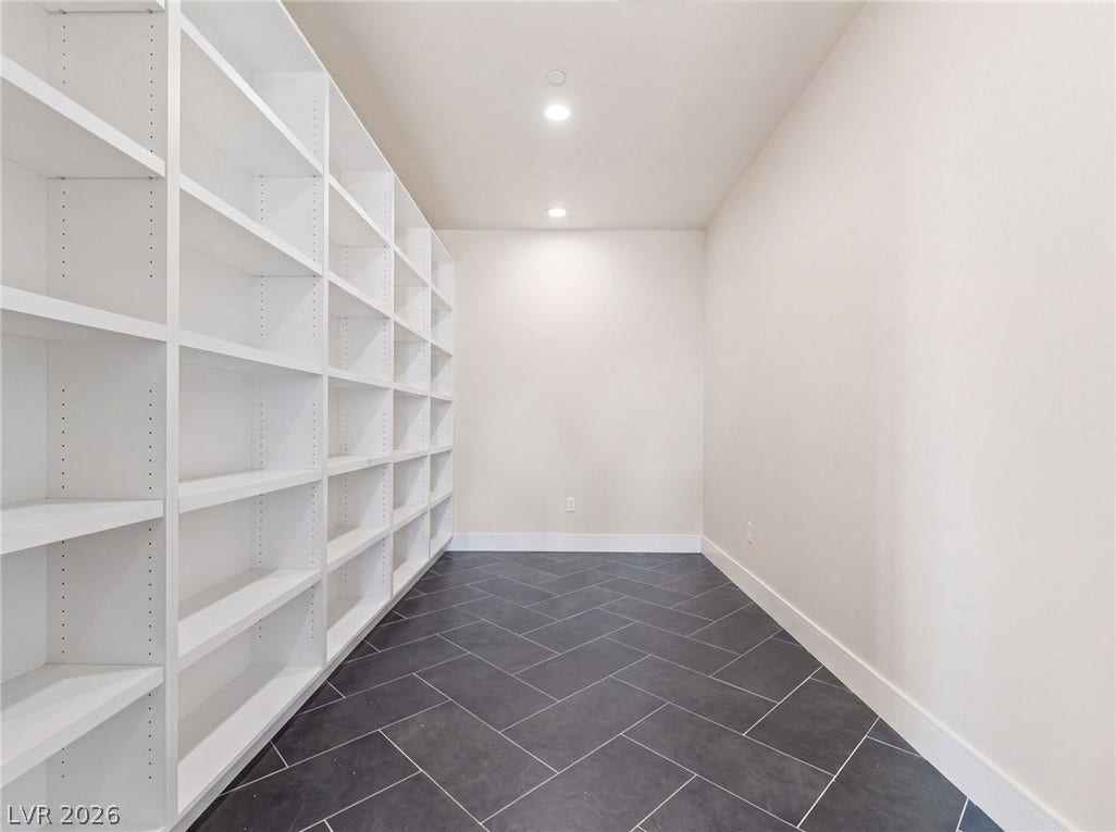 A spacious pantry area features custom built-in shelving and classic herringbone tile floors.