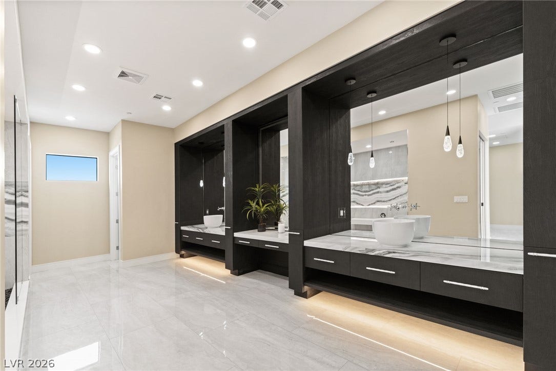 Gleaming stone tile floors anchor this master bathroom featuring customized floating vanities under recessed lights.
