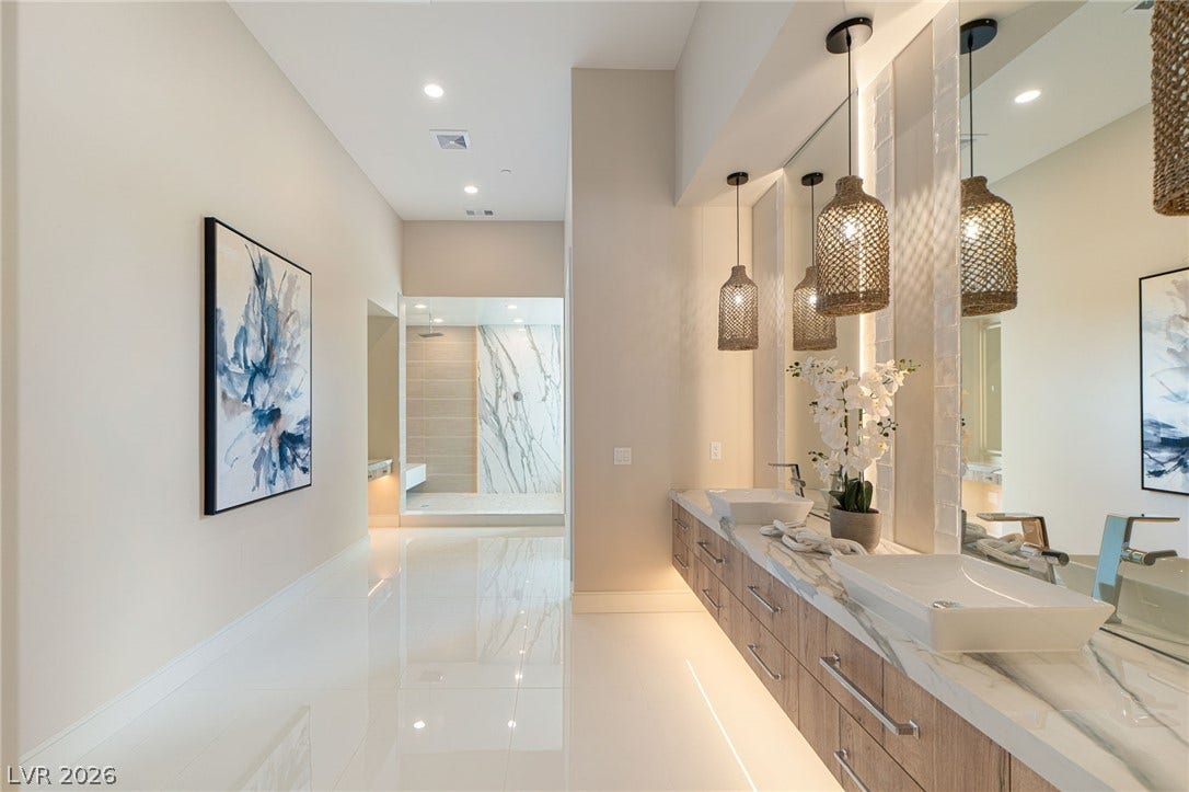 Gleaming polished tile floors lead past a modern double vanity toward a spacious walk-in shower.