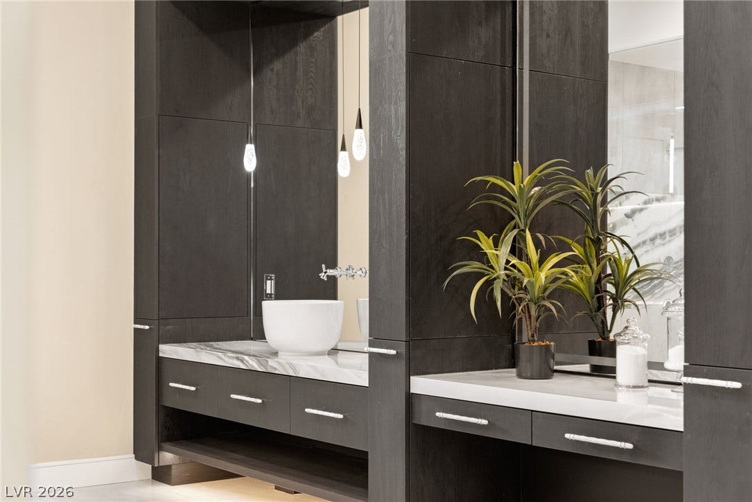 Rich dark wood cabinetry surrounds elegant stone vanities accented by modern vessel sinks.