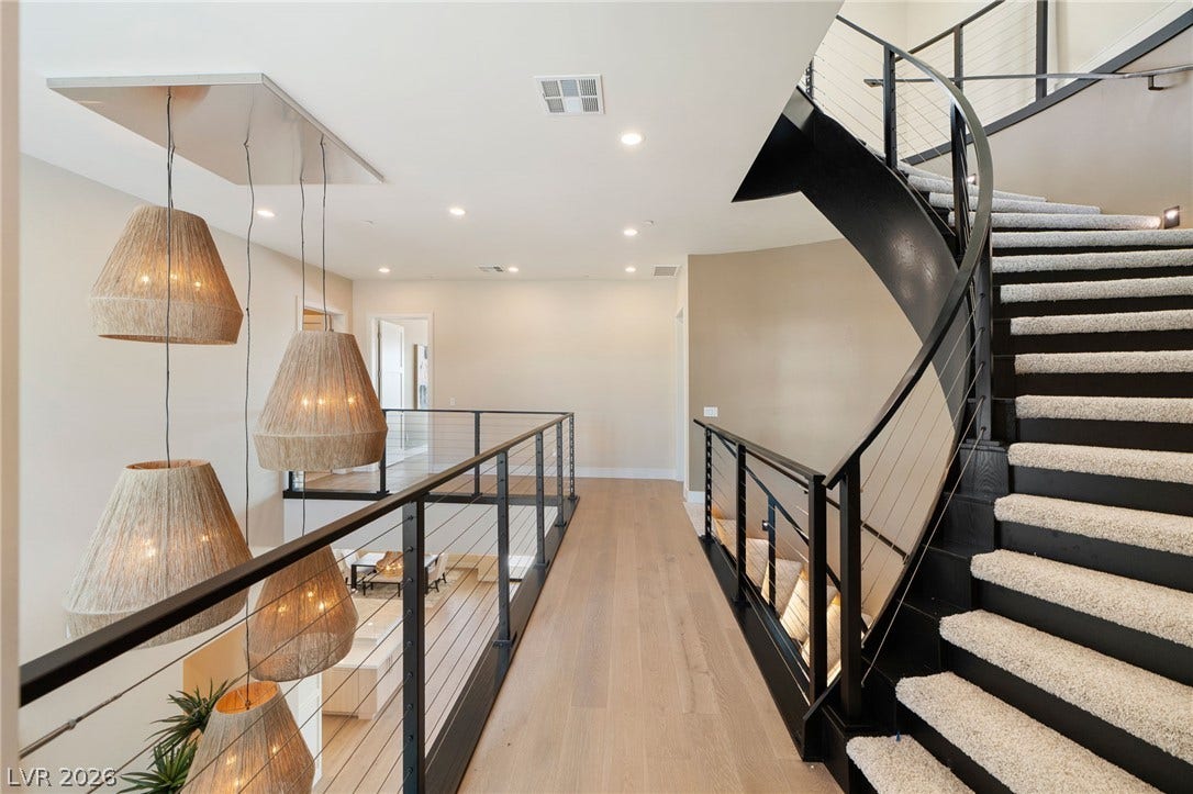 An elegant curved staircase anchors this open upper-level hallway featuring light wood flooring.