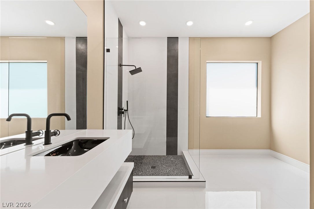 A glass-enclosed shower highlights this modern washroom featuring large-format tile flooring and minimalist architecture.