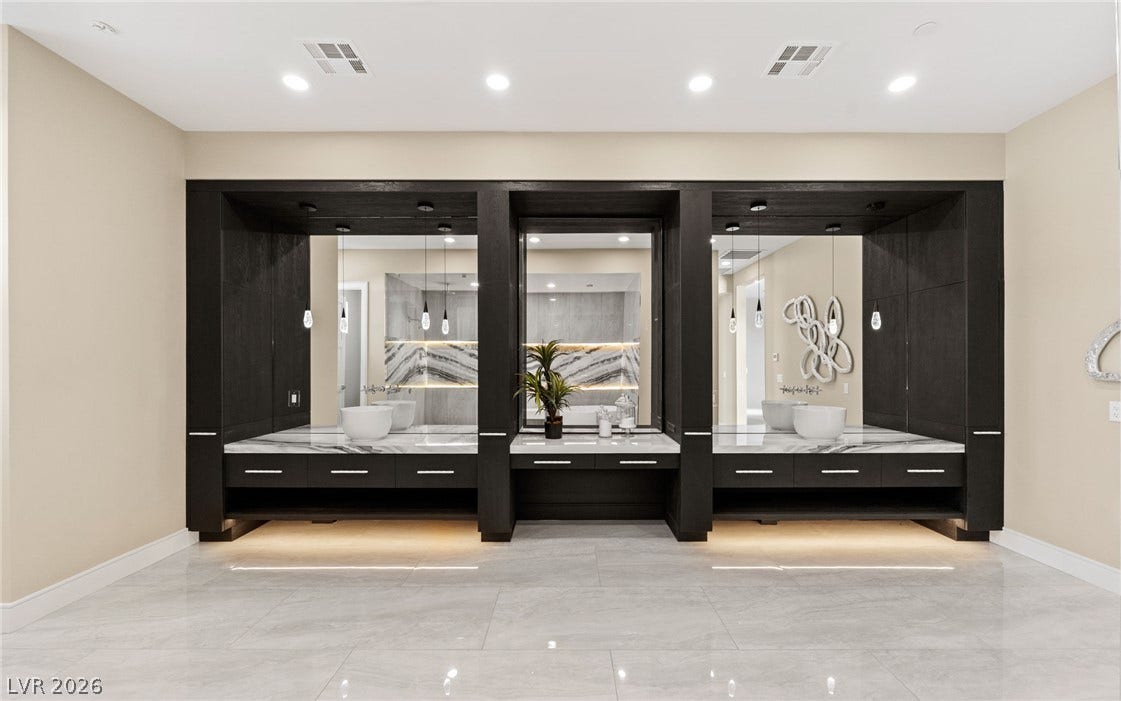 A spacious bathroom features polished tile floors and custom dark cabinetry with integrated lighting.
