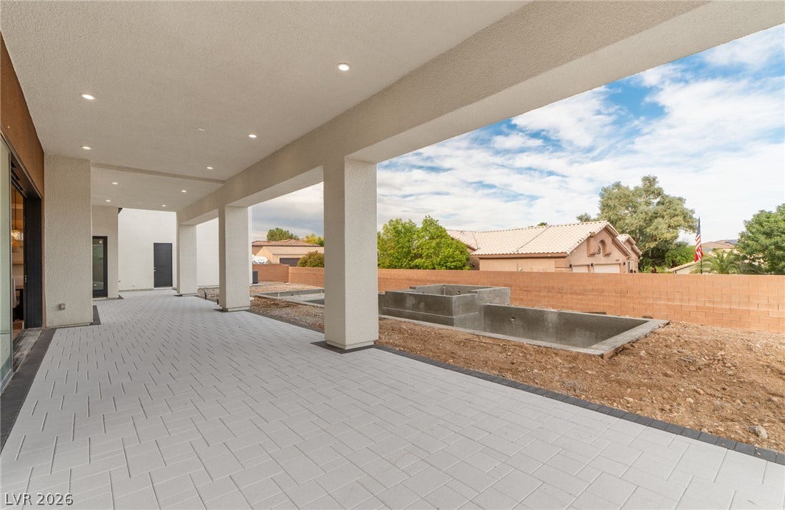 A spacious covered patio with paved flooring overlooks the backyard under construction.