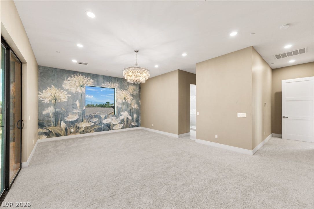 An elegant bedroom features plush carpeting, a sparkling chandelier, and sliding glass doors.