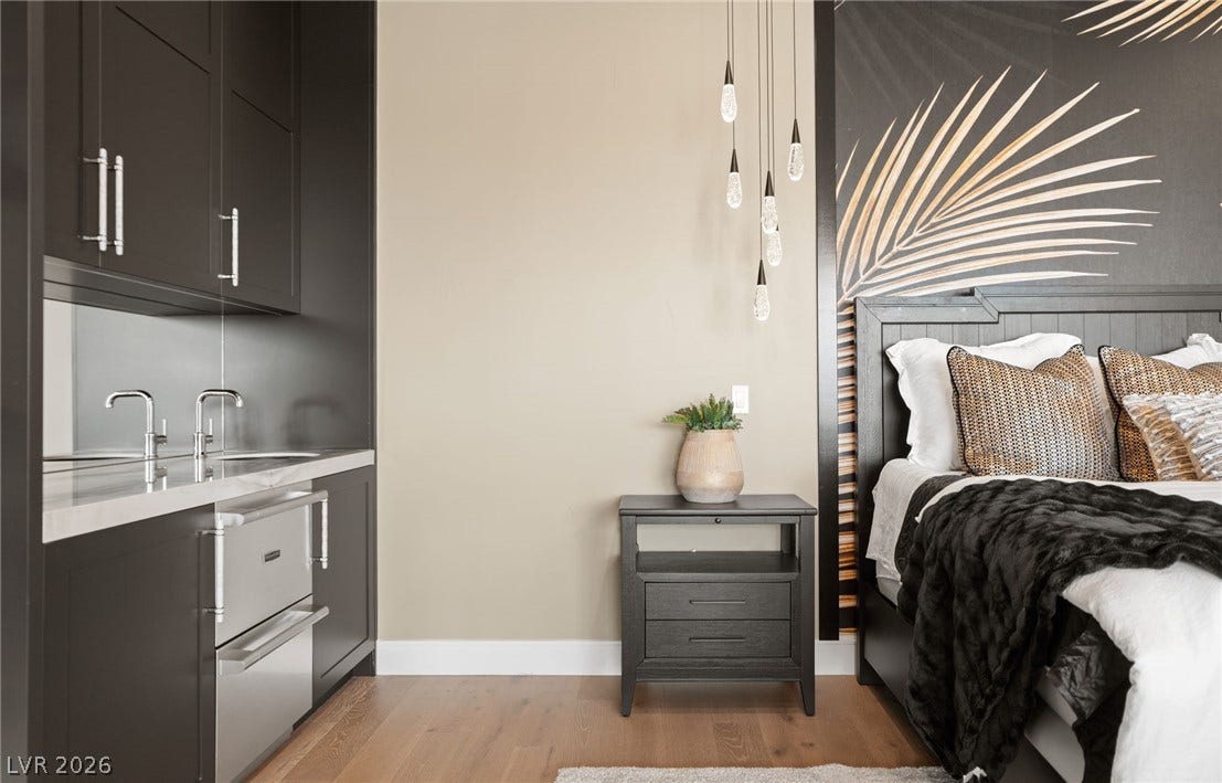 A built-in wet bar complements this modern bedroom suite featuring warm wood floors.