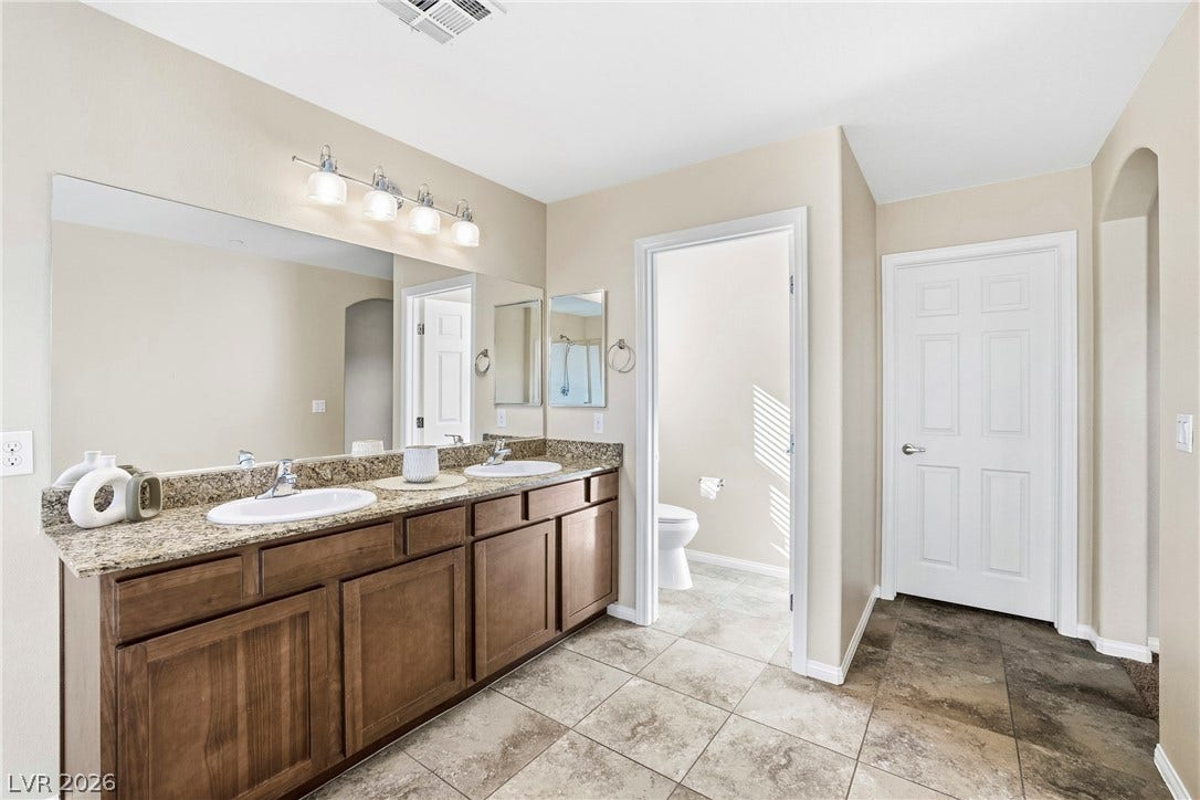 2221 Mundare Drive, Henderson, NV 89002 A spacious vanity with dual sinks and stone countertops anchors this tile-floored bathroom.