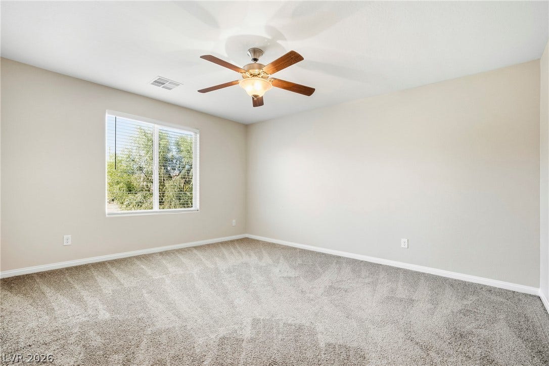2221 Mundare Drive, Henderson, NV 89002 Plush carpeting and a large window framing leafy green views define this comfortable bedroom.