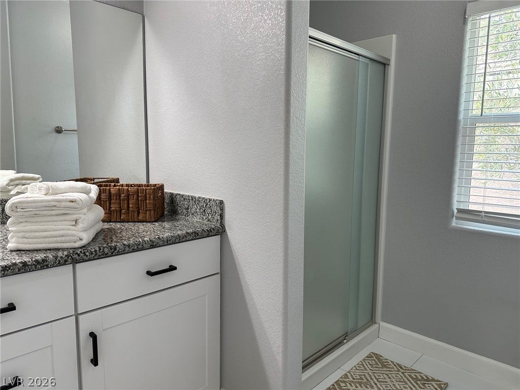 6089 Mustang Breeze Trail, #102, Henderson, NV 89011 Polished granite countertops complement the clean white cabinetry and walk-in shower in this bathroom.
