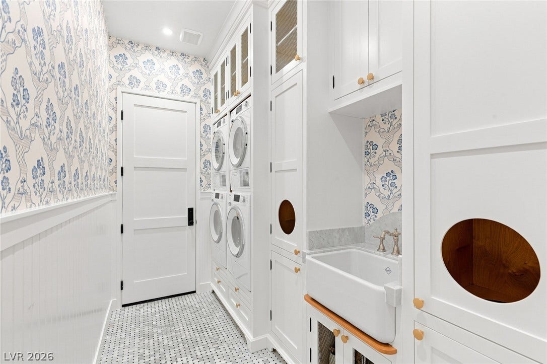 8 Pine Hollow Drive, Henderson, NV 89052 Custom cabinetry and wallpapered walls elevate this functional laundry space, featuring a built-in double washer-dryer station.