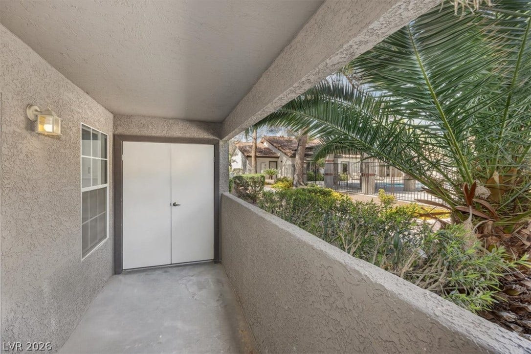 2606 S Durango Drive, #128, Las Vegas, NV 89117 Stucco half-walls frame a private concrete balcony overlooking lush tropical greenery.