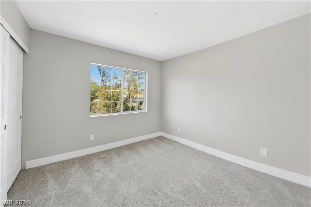 1906 Cardinal Point Street, Henderson, NV 89012 A spacious secondary bedroom features plush carpeting and a large multi-lite window framing tree views.