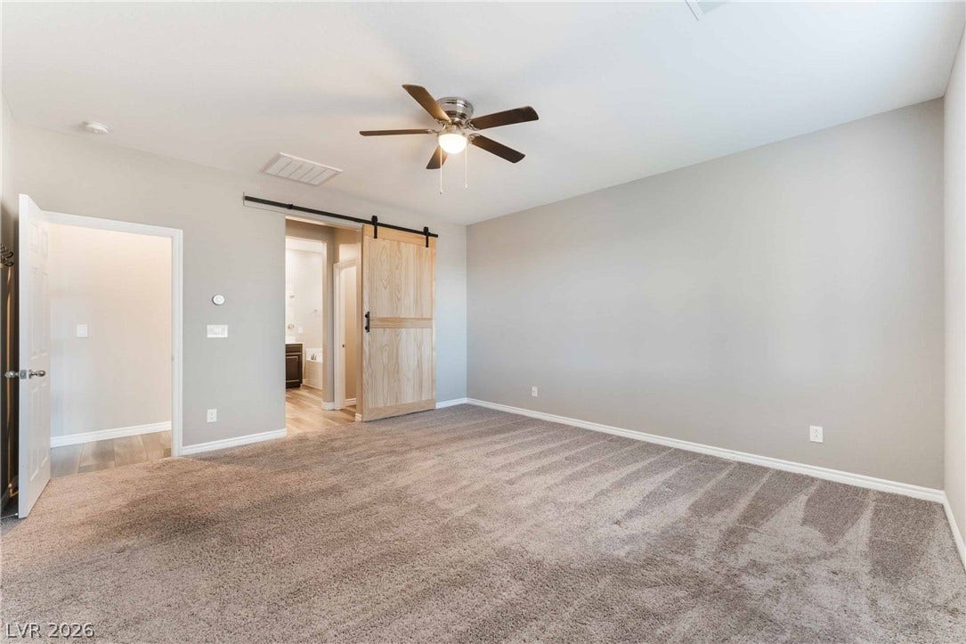 1430 Dire Wolf Avenue, North Las Vegas, NV 89084 Plush carpeting anchors this spacious bedroom featuring a rustic sliding barn door entryway.