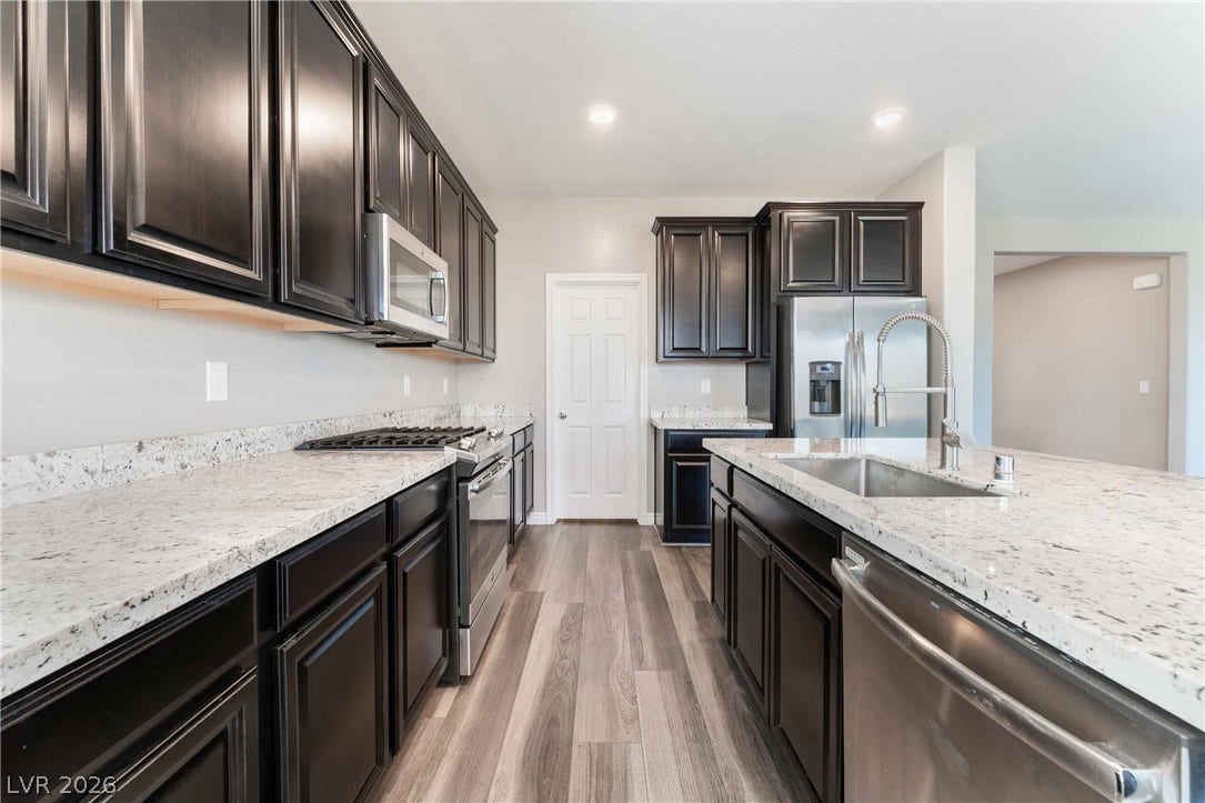 1430 Dire Wolf Avenue, North Las Vegas, NV 89084 Gleaming stone countertops and dark wood cabinetry define this modern open-concept kitchen.
