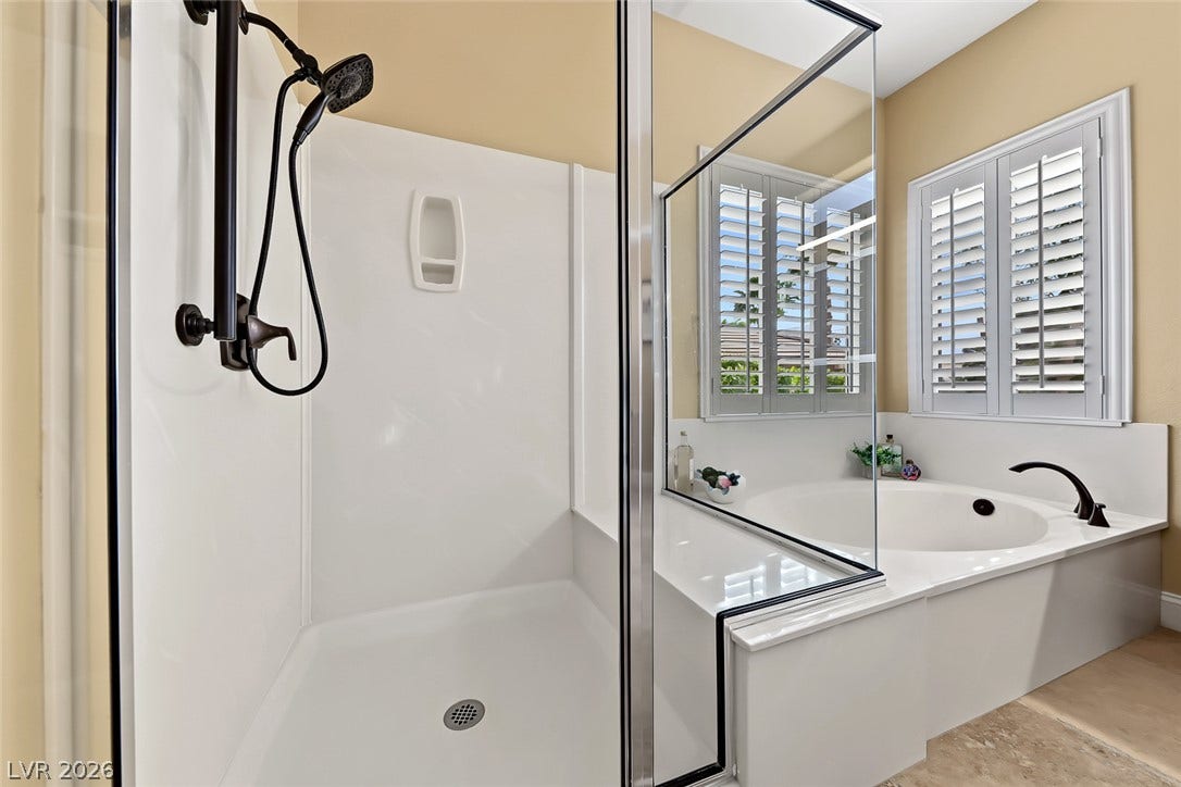 1646 Sebring Hills Drive, Henderson, NV 89052 A glass-enclosed shower stands alongside a deep soaking tub beneath classic plantation shutters.