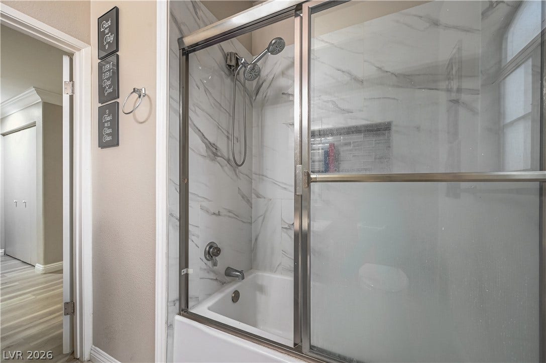 5415 W Harmon Avenue, #1029, Las Vegas, NV 89103 A glass-enclosed shower and tub combination features elegant marble-patterned wall tiling.