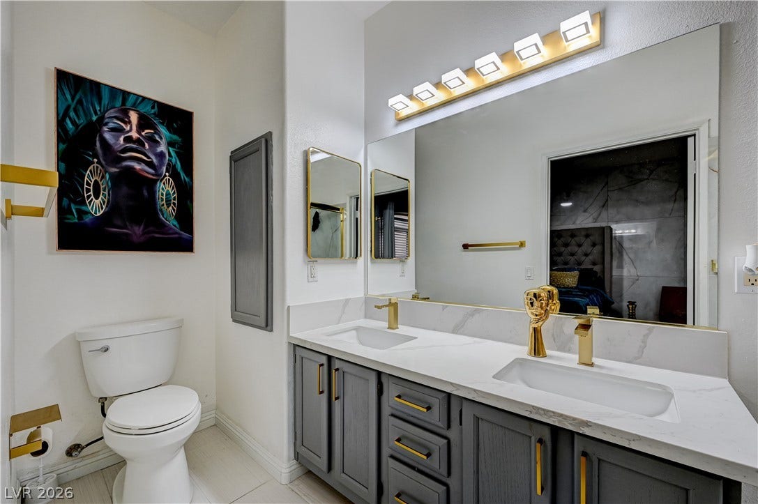 5415 W Harmon Avenue, #1029, Las Vegas, NV 89103 Gold fixtures accent a sleek double vanity topped with stone counters in this modern bathroom.