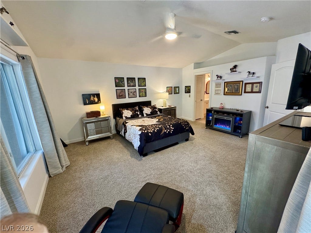 7652 Rolling View Drive, #202, Las Vegas, NV 89149 Plush carpeting anchors this spacious primary bedroom featuring vaulted ceilings and a modern fireplace unit.