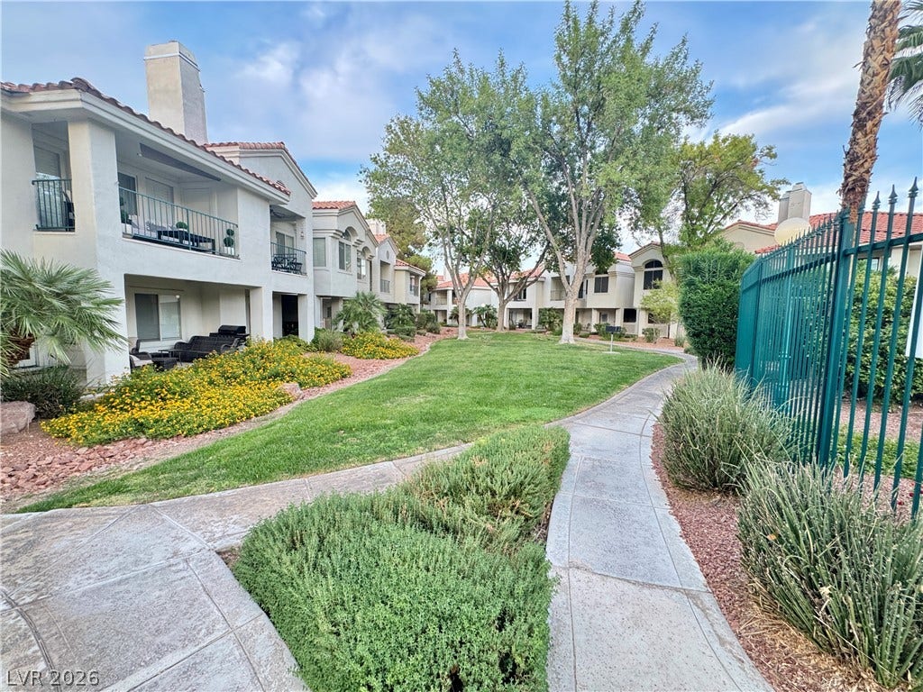 7652 Rolling View Drive, #202, Las Vegas, NV 89149 A curved concrete walkway winds past manicured lawns, mature shade trees, and stucco residences.