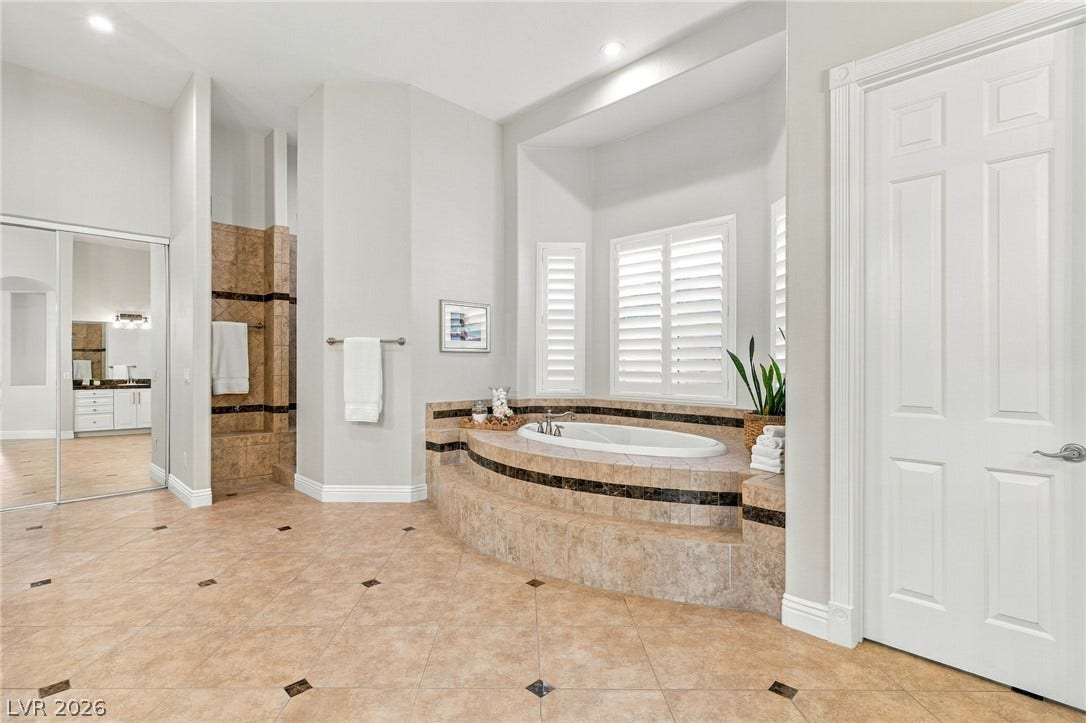 210 Torrey Morgan Way, Henderson, NV 89074 A raised soaking tub sits beneath plantation shutters in this tiled bathroom retreat.