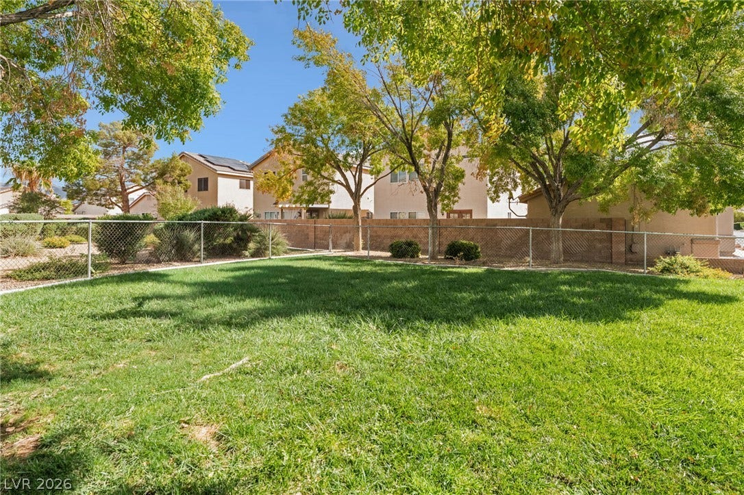 5348 Reardon Court, North Las Vegas, NV 89031 Mature trees shade a grassy lawn bordered by chain-link fencing under a clear blue sky.