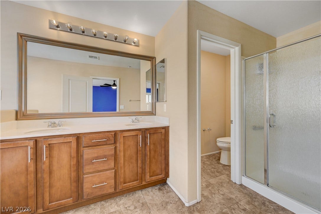 2088 Artistic Flair Walk, Henderson, NV 89044 Double vanities with warm wood cabinetry complement a glass-enclosed walk-in shower.