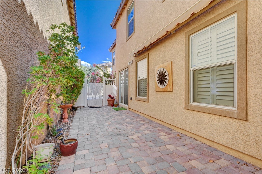 2088 Artistic Flair Walk, Henderson, NV 89044 An inviting paved courtyard pathway runs alongside the stucco exterior under clear blue skies.