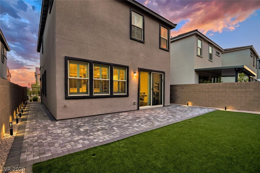 An inviting stone paver patio adjoins a manicured lawn under a vibrant sunset sky.