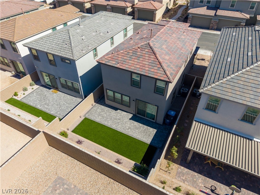 An aerial view showcases a modern two-story home with a paved patio and stone privacy wall.