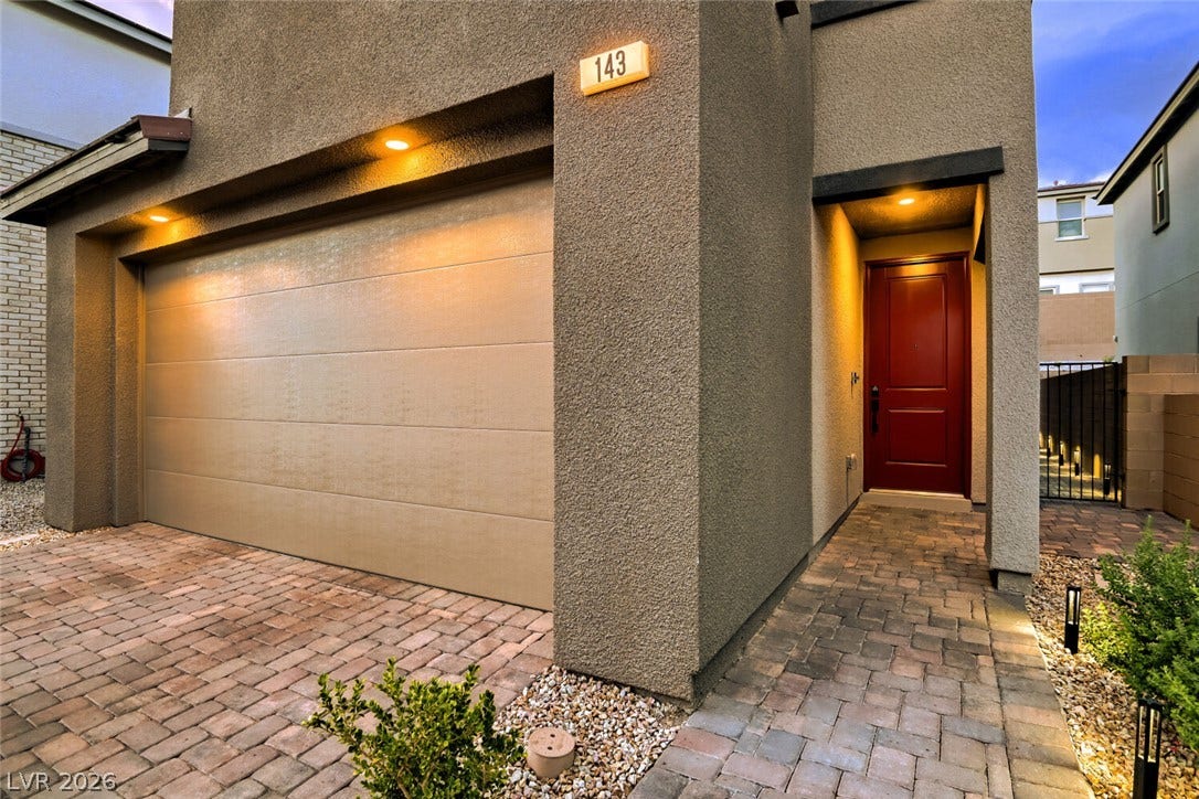 An inviting stucco entryway and paver driveway lead to the modern front door.