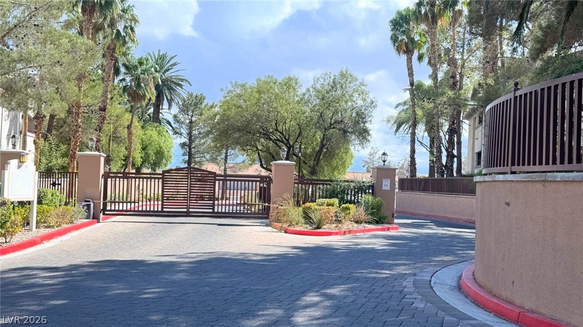 8304 Apple Glaze Avenue, #203, Las Vegas, NV 89145 Secure gated entry features a brick-paved driveway flanked by mature palm trees.