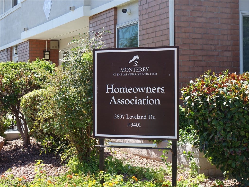 769 Oakmont Avenue, #403, Las Vegas, NV 89109 A prominent community sign stands nestled among mature greenery against a brick exterior.